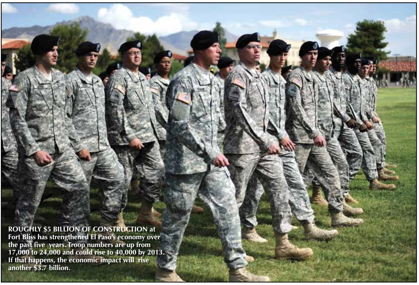 This image shows a group of soldiers in Army Combat Uniforms and berets marching in formation on a grassy field at Fort Bliss, with trees, mountains, and buildings in the background under a partly cloudy sky. The accompanying text notes that approximately $5 billion of construction at Fort Bliss has boosted El Pasoโs economy over the past five years. Troop numbers have grown from 17,000 to 24,000 and could reach 40,000 by 2013, which would add another $3.7 billion to the economic impact. The scene captures the scale and discipline of the military presence that has become a significant economic driver for the region.
