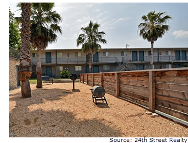 The gravel-paved grilling area of Romeria Place in the late afternoon. It is bordered by a wooden fence and palm trees