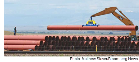 A stack of sections of pipeline, with a man standing on top directing activity.